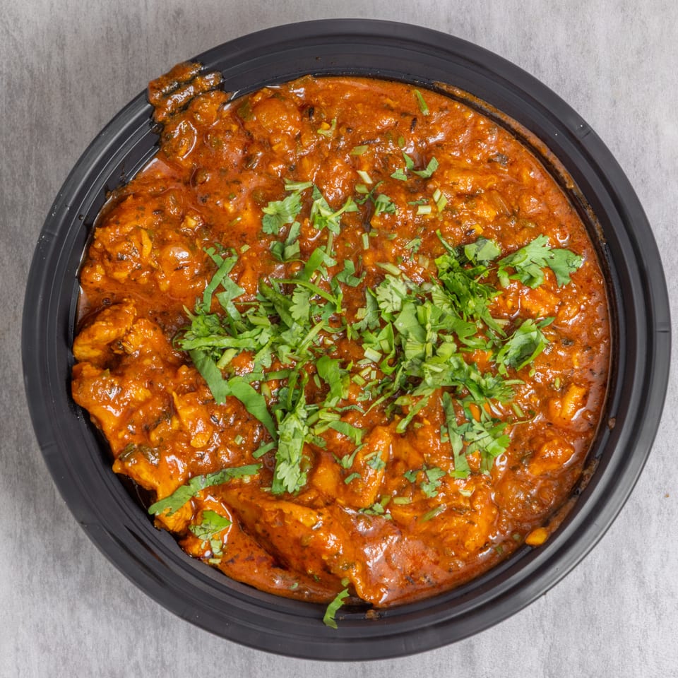 Close-up of creamy orange curry with chunks of meat, garnished with fresh cilantro in a black bowl.