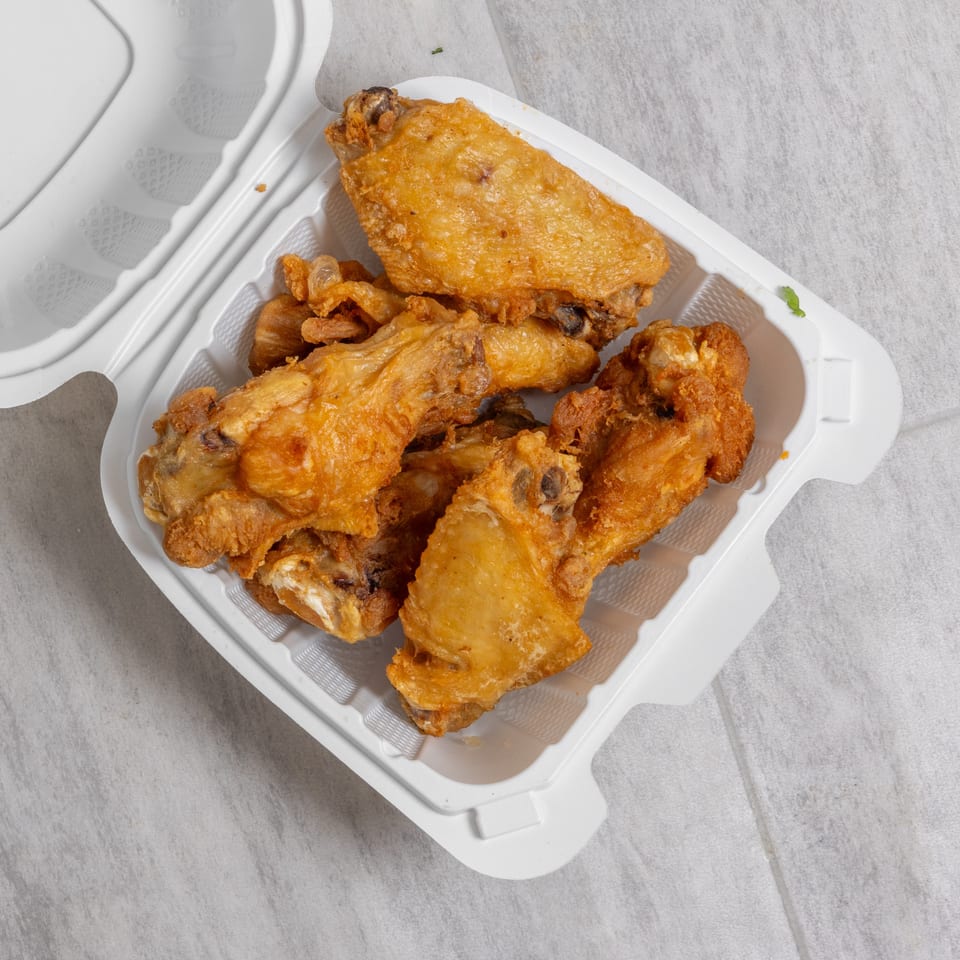 Crispy golden fried chicken wings piled in an open white takeout container.